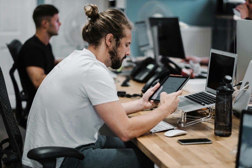 IT support engineer working across laptop and tablet in a busy office