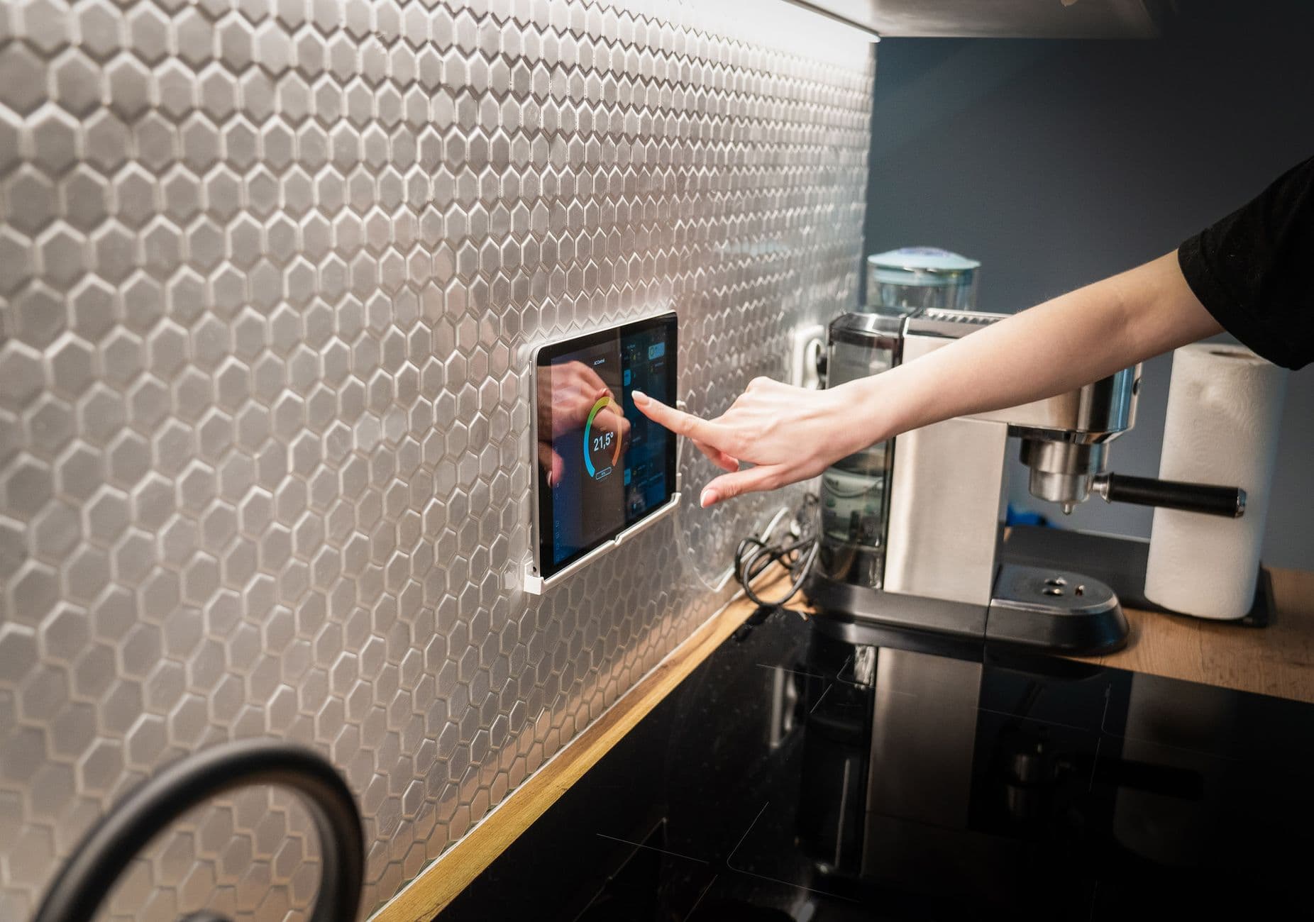 A touchscreen smart home control panel integrated into a modern kitchen wall