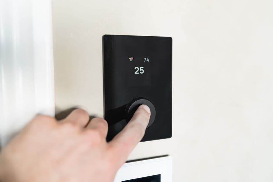 A hand adjusting a sleek smart thermostat on a wall